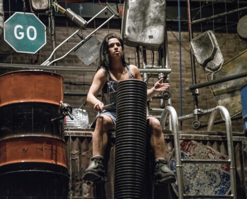 A woman performing in STOMP seated while drumming