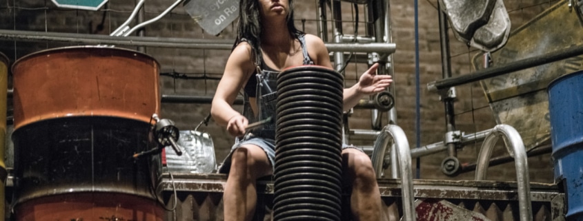 A woman performing in STOMP seated while drumming