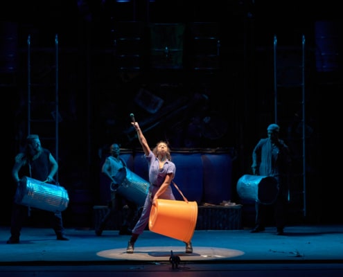 The cast of STOMP performs with large buckets