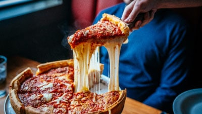 Image of a super cheesey pizza sliced being lifted in the air 