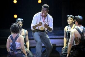 A man sings in the center of a group in Hadestown