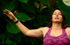 A woman sits in a pose in front of lush greenery