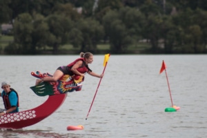 A woman leans over the edge of a boat to pick up a flag