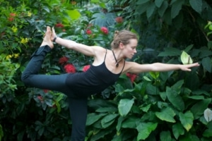 A woman performs a yoga pose in front of lush greenery