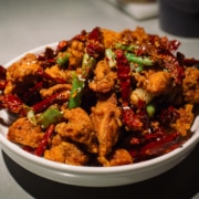 A bowl of Chinese food with meat, green onions, and peppers