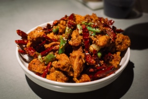 A bowl of Chinese food with meat, green onions, and peppers