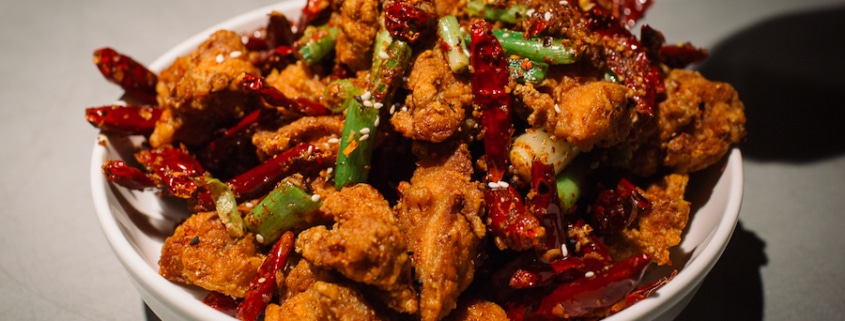 A bowl of Chinese food with meat, green onions, and peppers