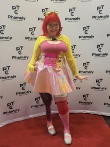 An actress in colorful costume poses in front of a banner