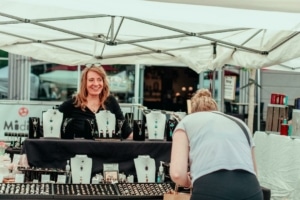 A woman selling jewelry smiles as a customer examines her table