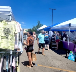 People walk past booths in an outdoor market