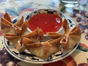 A plate of crab rangoons with sweet and sour sauce