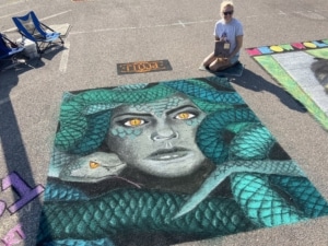 A woman sits next to her chalk art of Medusa