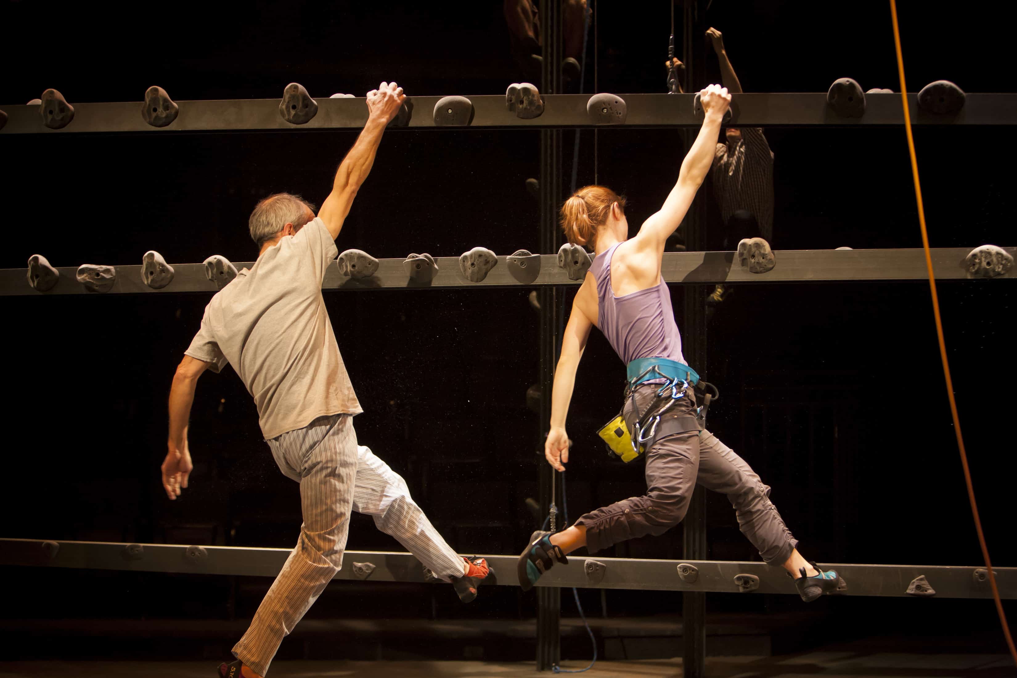 A man and a woman in climbing gear hang on to a rock wall in Grace, Or the Art of Climbing.