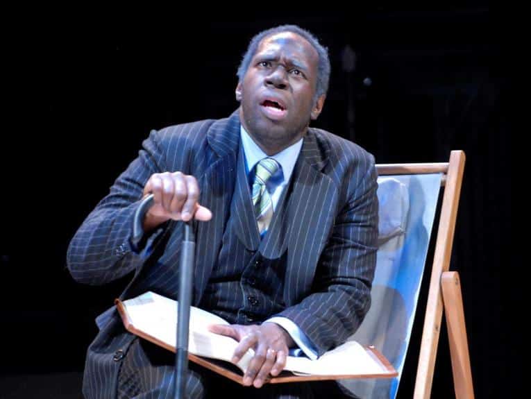 An older man sits in a chair with a large book in 1001.