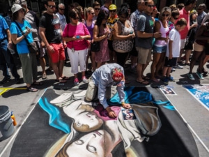 A large group of people pass a man working on chalk art