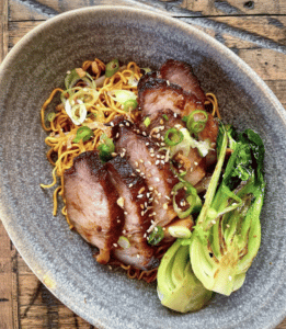 A plate of sliced meat with bok choy and noodles