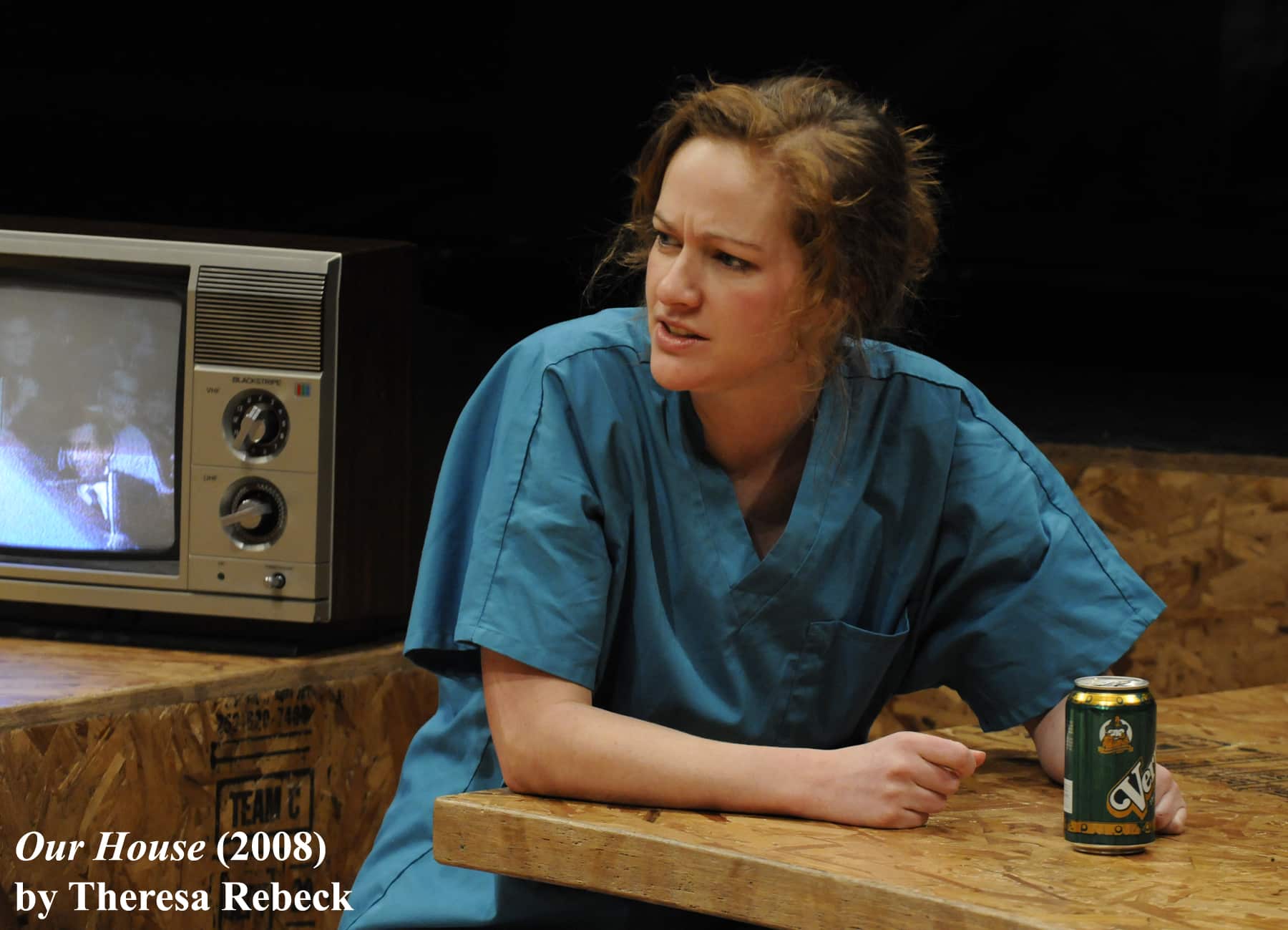 A woman wearing scrubs sits at a table with a beer in Our House.