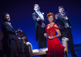 A woman in a red dress smiles as men in black tie reach for her in The Unsinkable Molly Brown