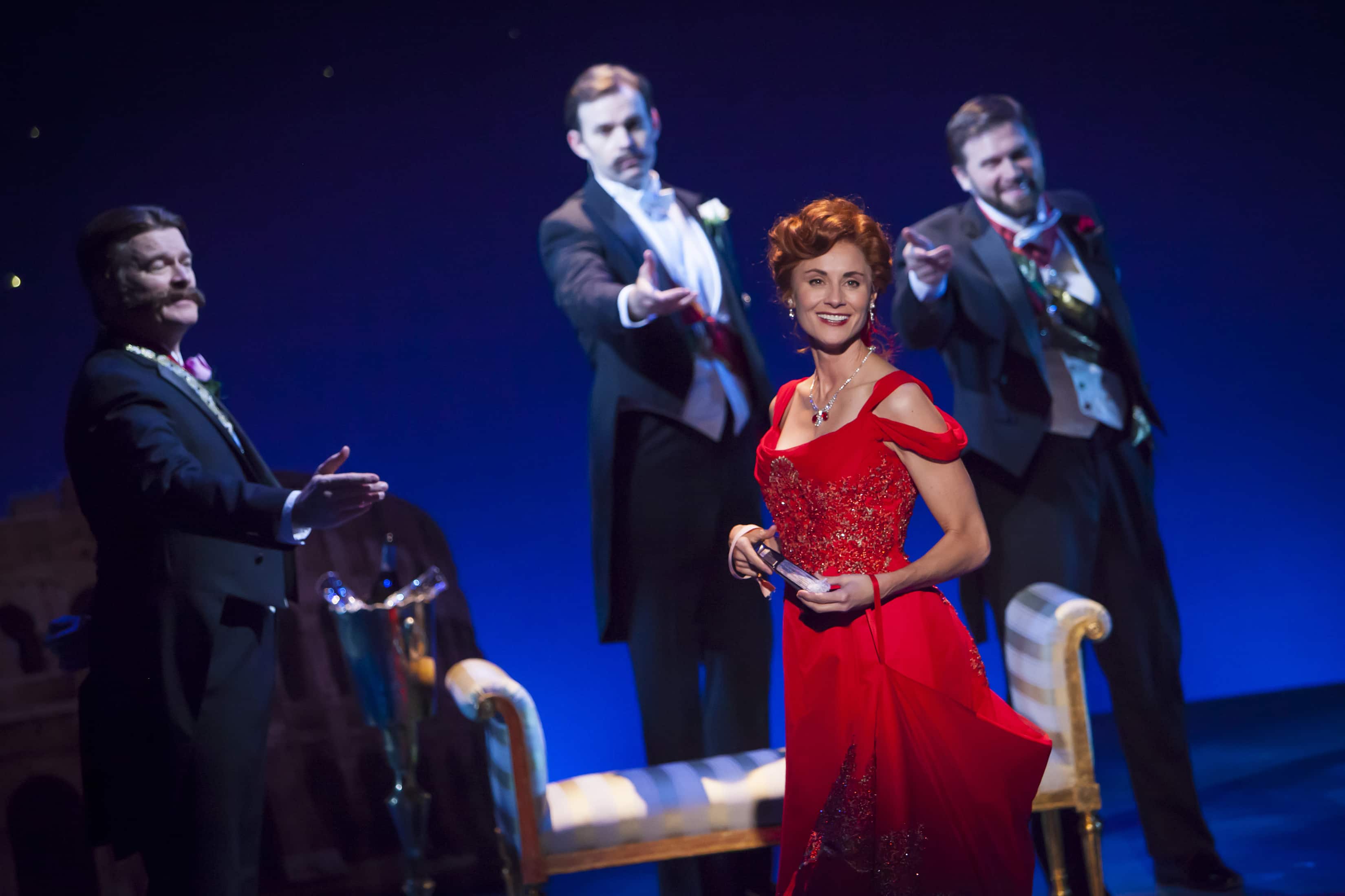 A woman in a red dress smiles as men in black tie reach for her in The Unsinkable Molly Brown