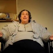 An overweight man is seated in a chair in The Whale.