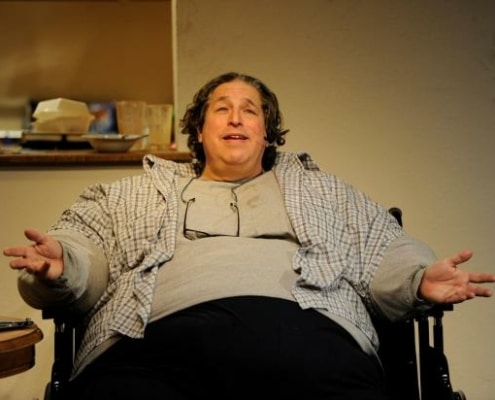 An overweight man is seated in a chair in The Whale.