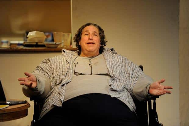 An overweight man is seated in a chair in The Whale.