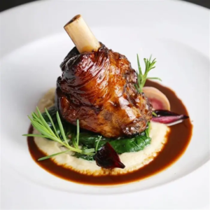 A lamb shank surrounded by sauce and herbs