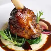 A lamb shank surrounded by sauce and herbs