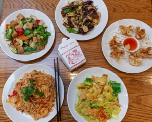 Five different plates of Chinese food with a takeout box in the center