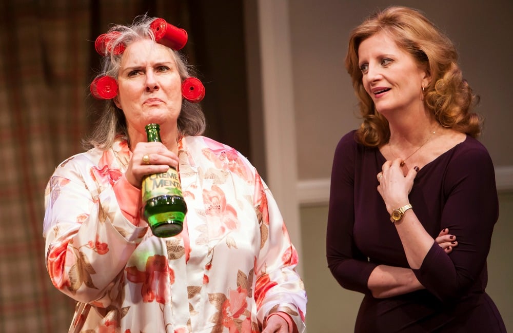 An older woman in a robe and hair curlers drinks from a bottle while a younger woman watches in The Most Deserving.