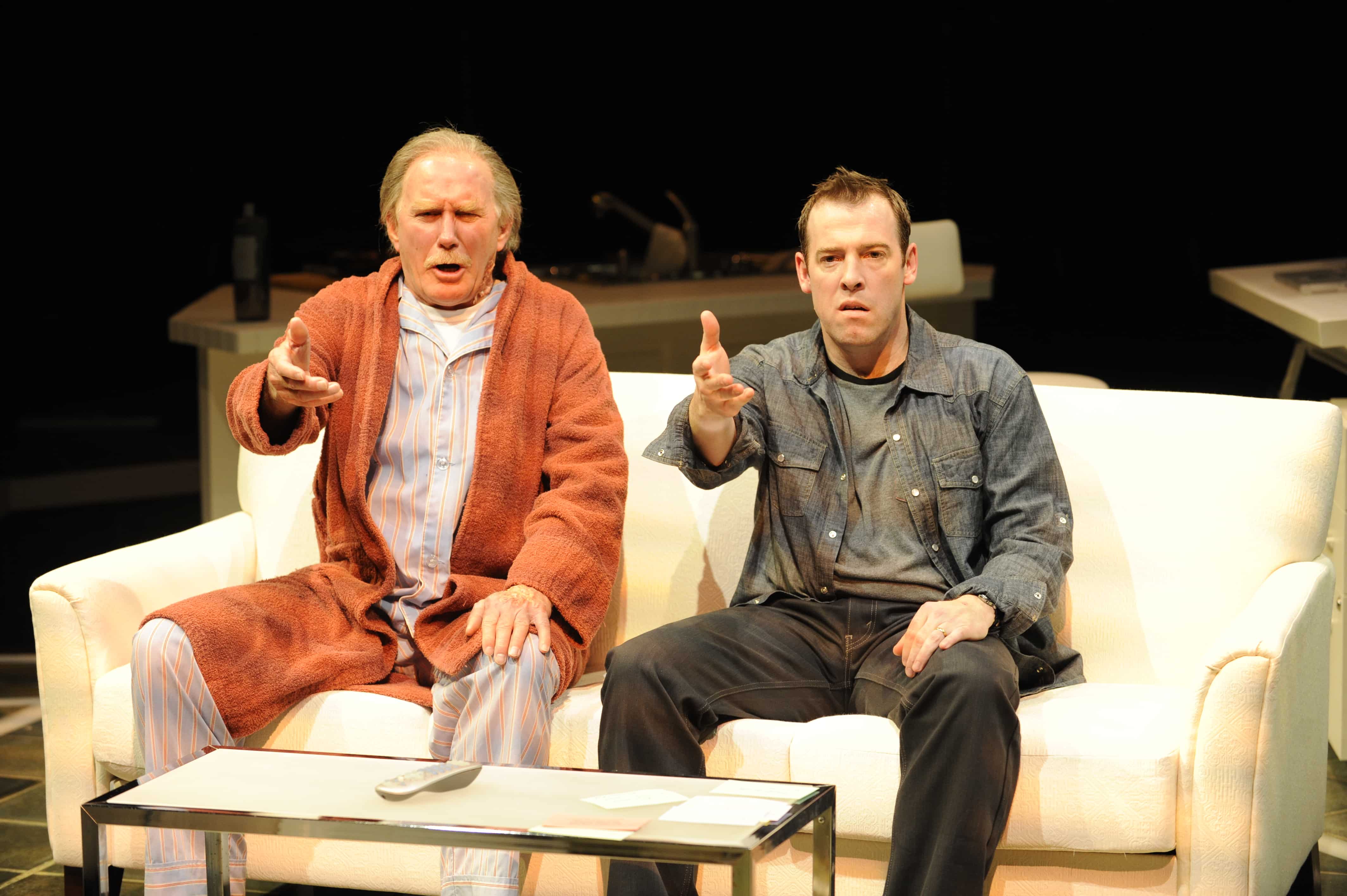 Two men sit on a couch gesturing to something in front of them in The Catch.