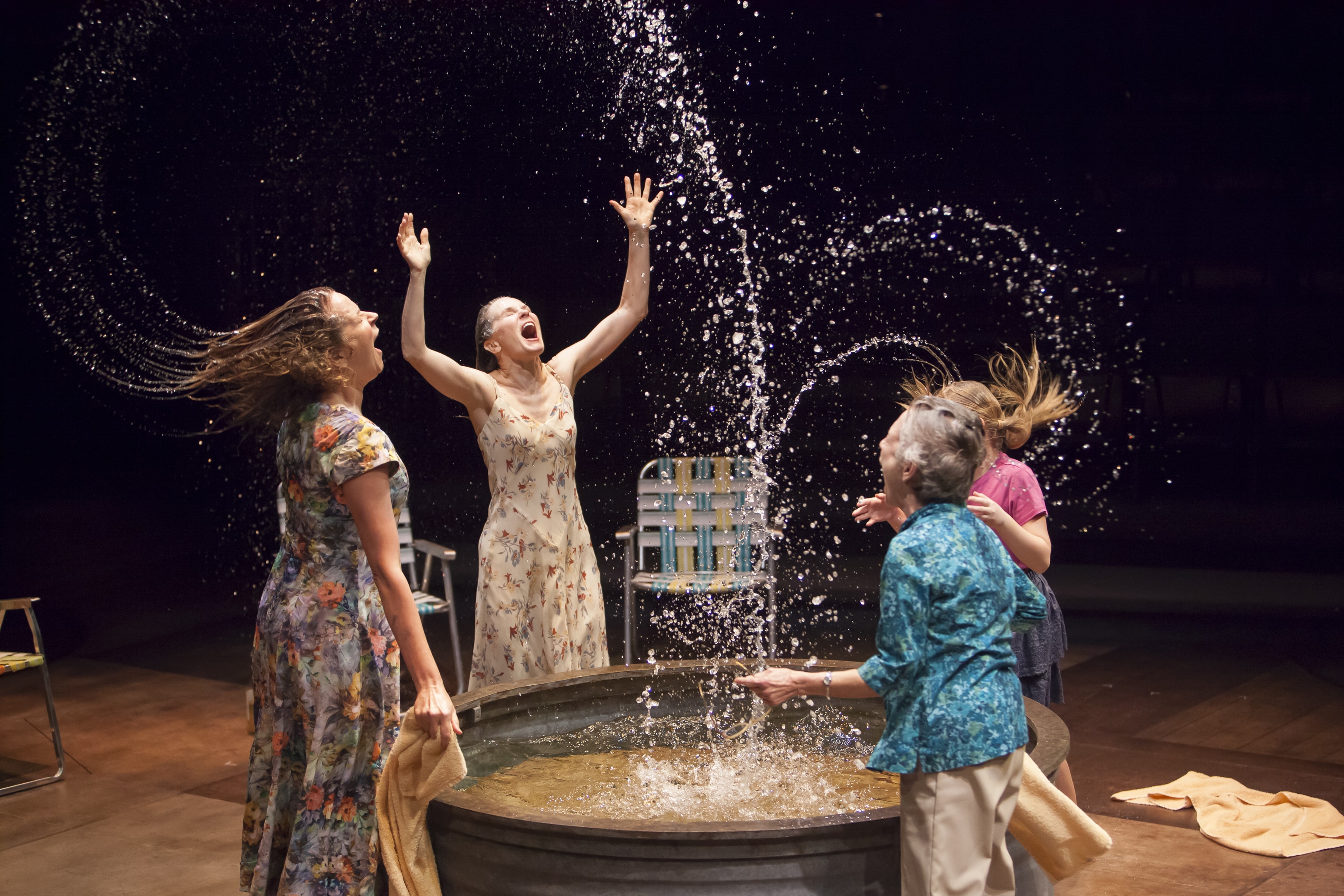 Two women and two children play in a small pool, splashing water high into the air in Benediction.