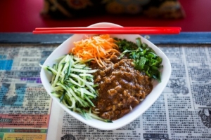 A bowl of Chinese food with meat, cilantro, shredded carrot and cucumber