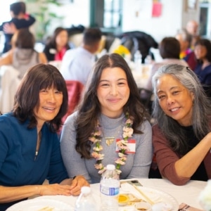 Three people are smiling seated at a table