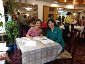 Two women are seated at a table and smile