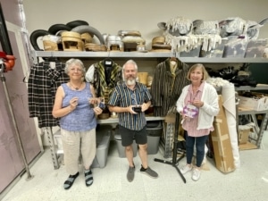 Three members of the costume shop pose with costumes and items belonging to Cathie Gagnon