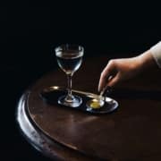 A glass sits on a tray while a hand reaches for it