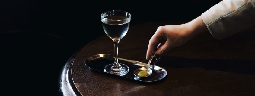 A glass sits on a tray while a hand reaches for it