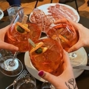 Glasses filled with orange cocktails are toasted in the center of a table