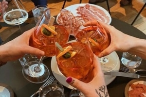 Glasses filled with orange cocktails are toasted in the center of a table