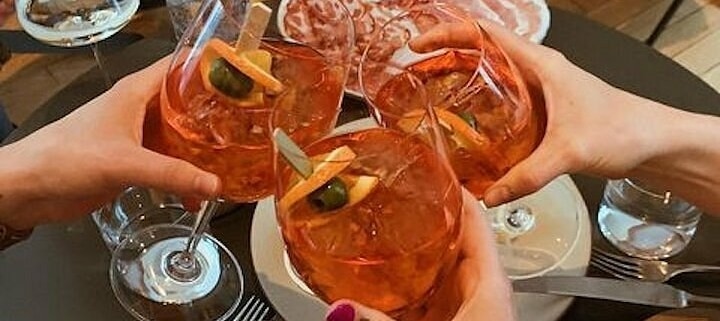 Glasses filled with orange cocktails are toasted in the center of a table