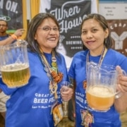 Two volunteers stand together for a photo holding pitchers of beer