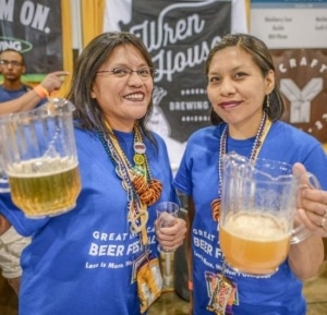 Two volunteers stand together for a photo holding pitchers of beer