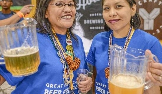 Two volunteers stand together for a photo holding pitchers of beer