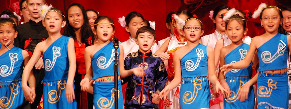 A group of children wearing detailed costumes sing onstage