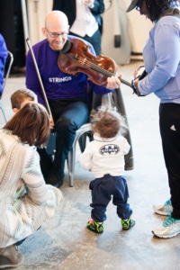 A child watches as a musician holds up his violin