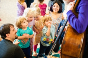 Children crowd around a musician with a cello