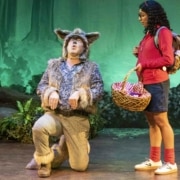 A girl watches as an actor dressed as a wolf kneels and howls