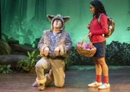 A girl watches as an actor dressed as a wolf kneels and howls