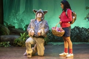 A girl watches as an actor dressed as a wolf kneels and howls